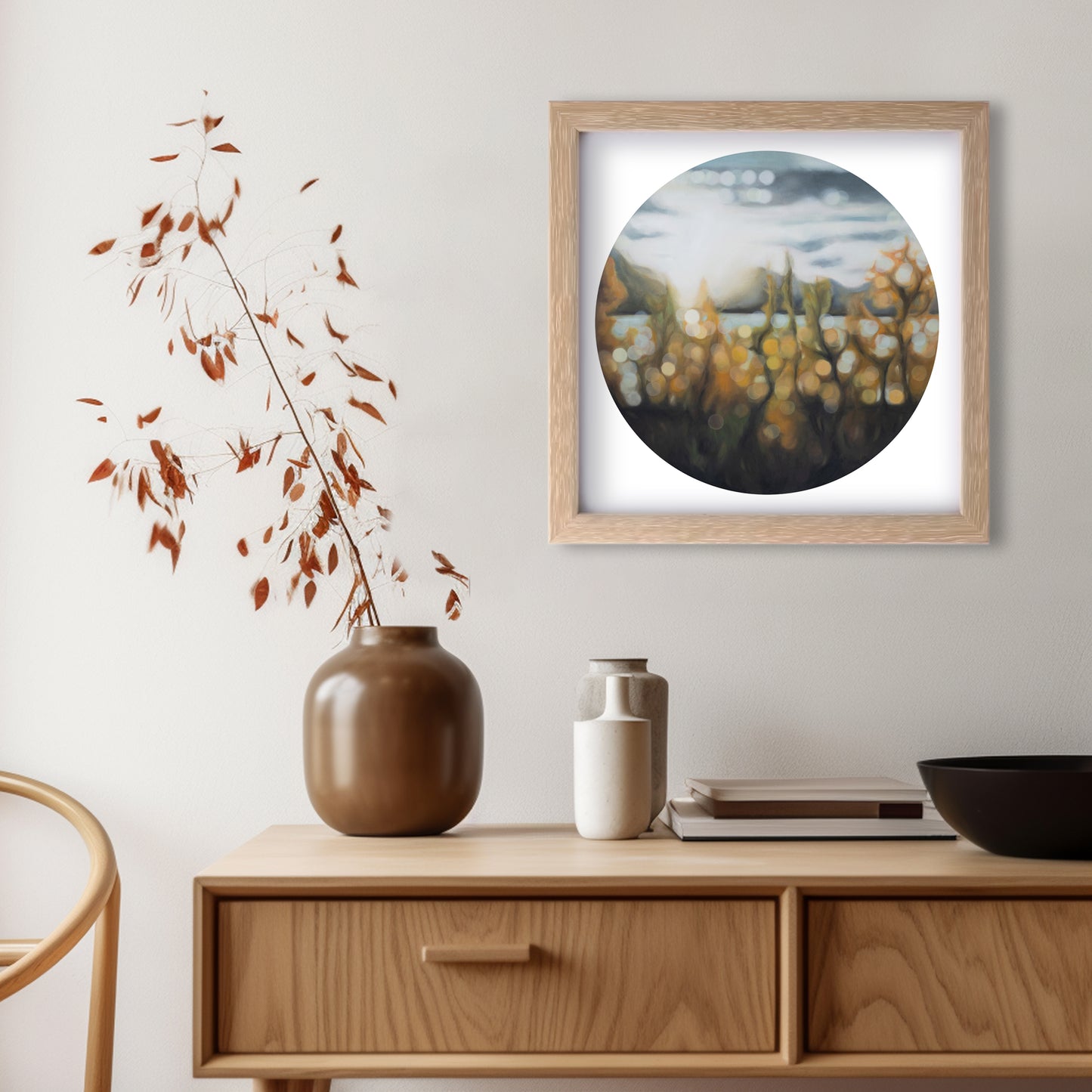 Wanaka lakefront, fine art print in a blurry bokeh style. Autumn light on Lake Wanaka, New Zealand. Painted by New Zealand artist Mel McKenzie. Orange and rust tones. Round art on a square print framed in a wooden frame and hanging above a wooden console in a dining room.