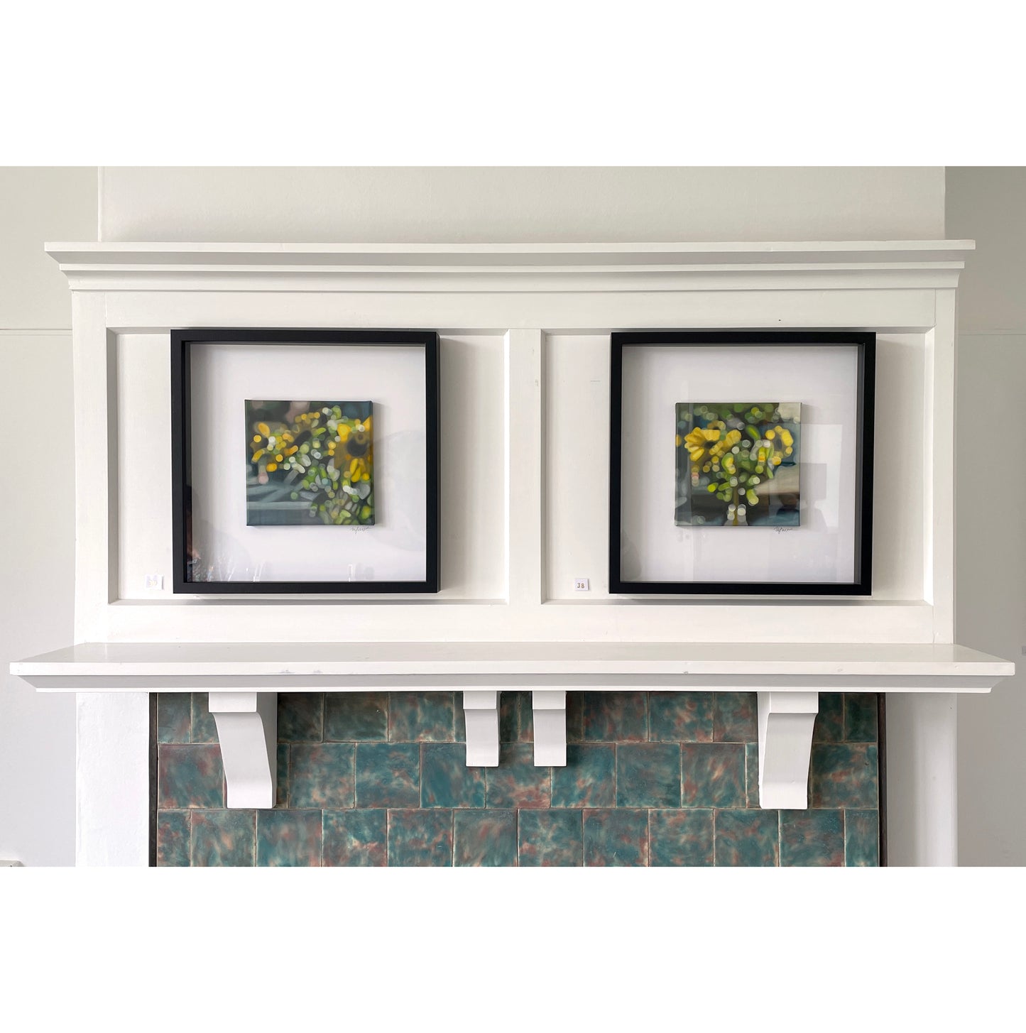 White mantelpiece with two framed pictures of flowers on a gray wall.