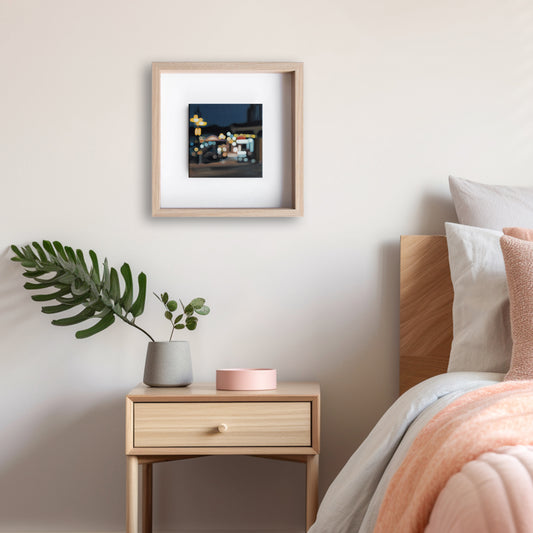 Wanaka New Zealand, lakefront drive cafe art hanging in bedroom. Painted in a blurry bokeh style on a small canvas framed in wood frame. Lights of the street and stores. Art by New Zealand artist Mel McKenzie, The Penny Drops.