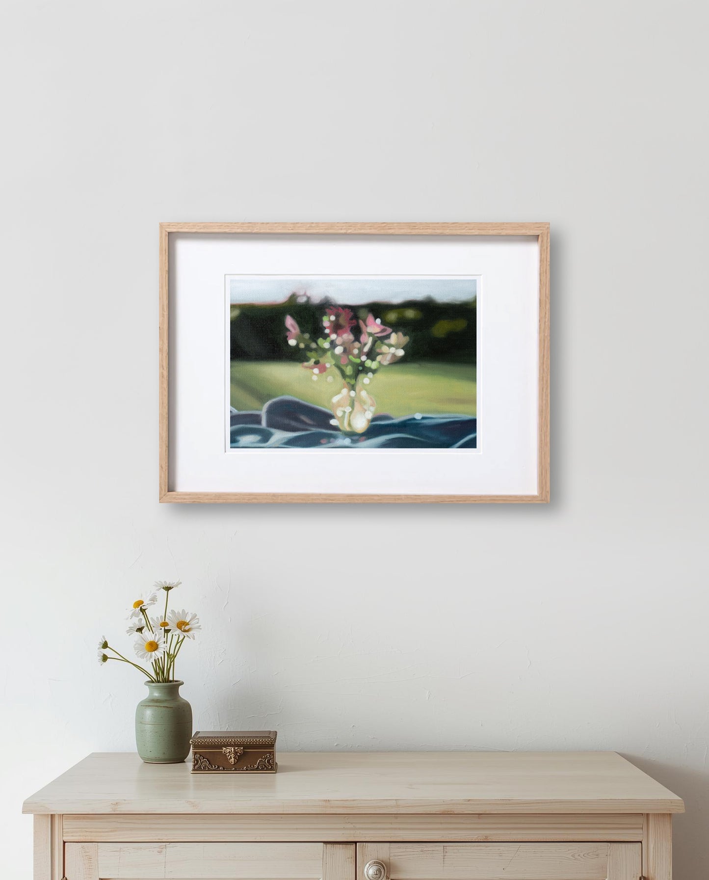 Framed photograph of flowers on a wall above a wooden cabinet with decorative items.