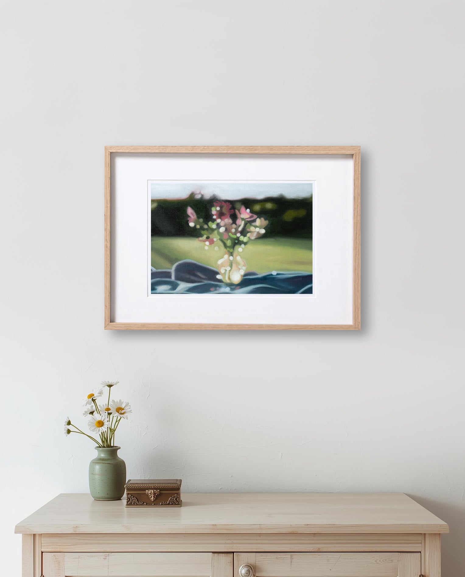 Framed photograph of flowers on a wall above a wooden cabinet with decorative items.