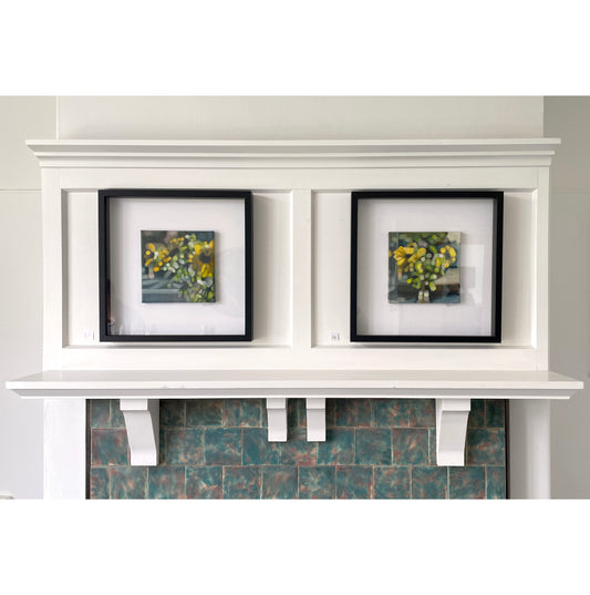 White mantelpiece with two framed pictures of flowers on a gray wall.